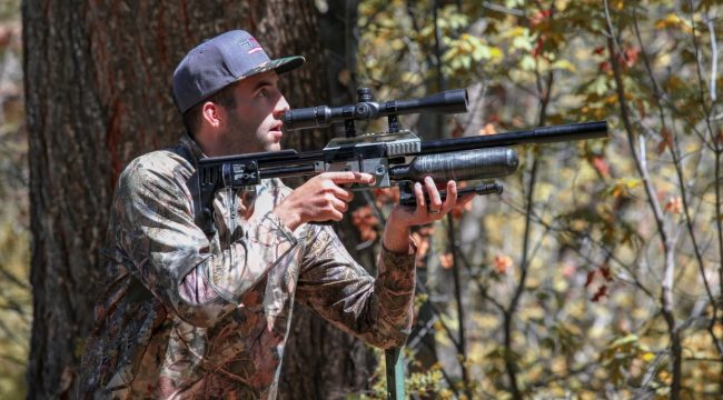 Hunter carrying an air rifle through the woods as he looks for prey.